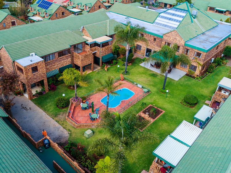 Aerial view of a residential complex featuring a central communal garden, swimming pool, paved patio areas, and brick buildings with green tiled roofs.