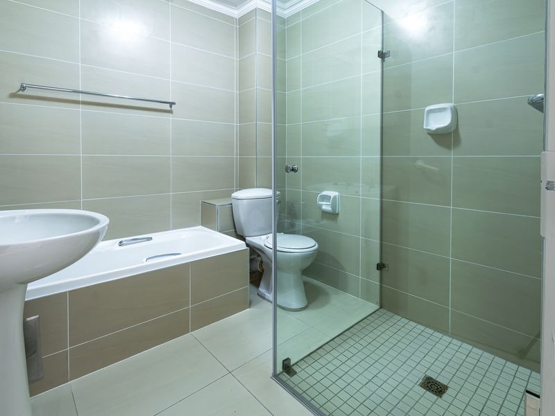 A functional bathroom featuring a pedestal basin, a built-in bathtub, and a separate glass-enclosed shower with neutral wall and floor tiling.