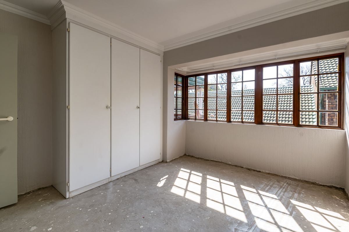 An empty bedroom featuring built-in cupboards, wooden frame windows, and unfinished concrete flooring, offering a blank canvas for renovation.