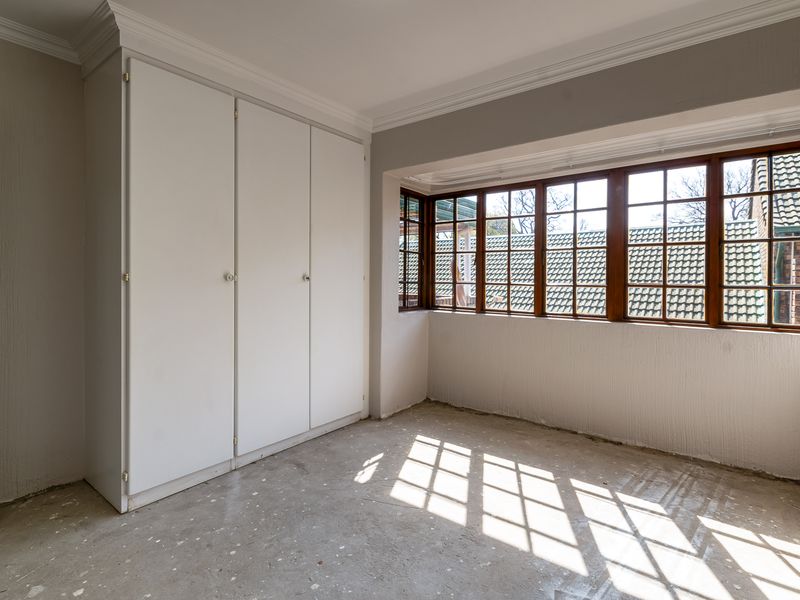 An empty bedroom featuring built-in cupboards, wooden frame windows, and unfinished concrete flooring, offering a blank canvas for renovation.