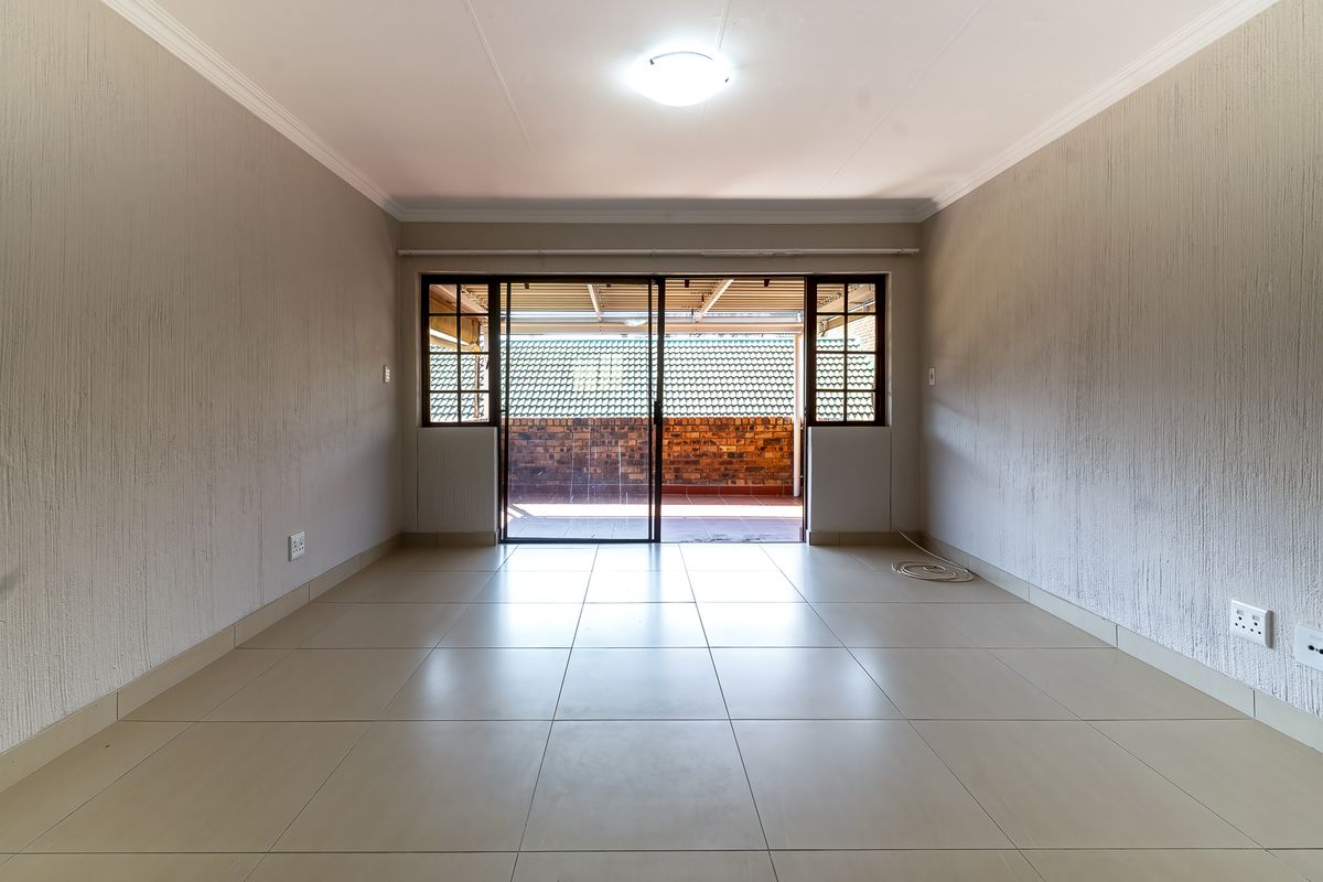 A bright, empty living room featuring neutral tiled flooring, textured walls, and a sliding glass door providing access to an outdoor patio area.