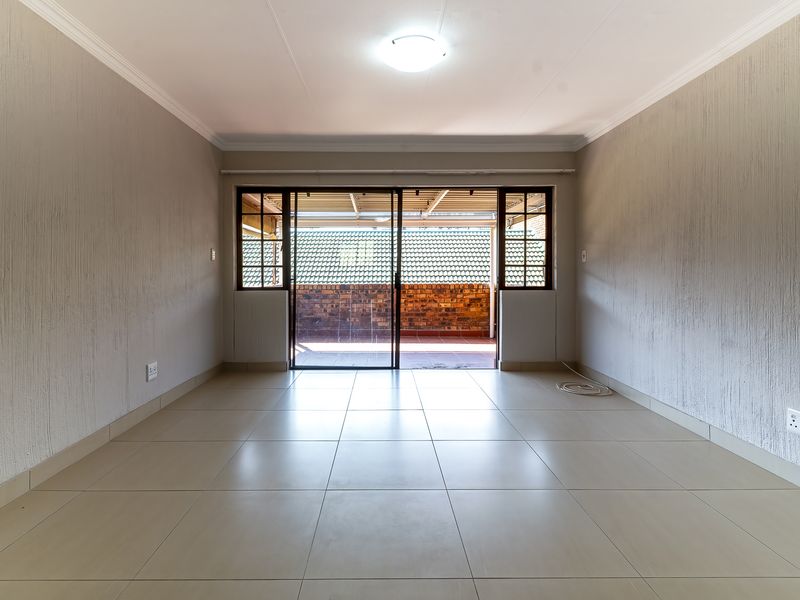 A bright, empty living room featuring neutral tiled flooring, textured walls, and a sliding glass door providing access to an outdoor patio area.