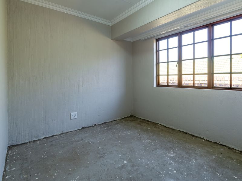 An empty bedroom featuring textured walls, coving, and a multi-pane window, currently requiring flooring installation and finishing touches.
