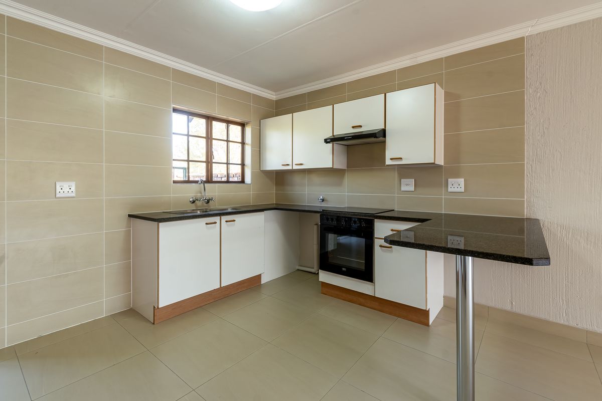 A clean, functional kitchen featuring white cabinetry, granite countertops, a breakfast bar, and built-in appliances, finished with neutral wall and floor tiles.