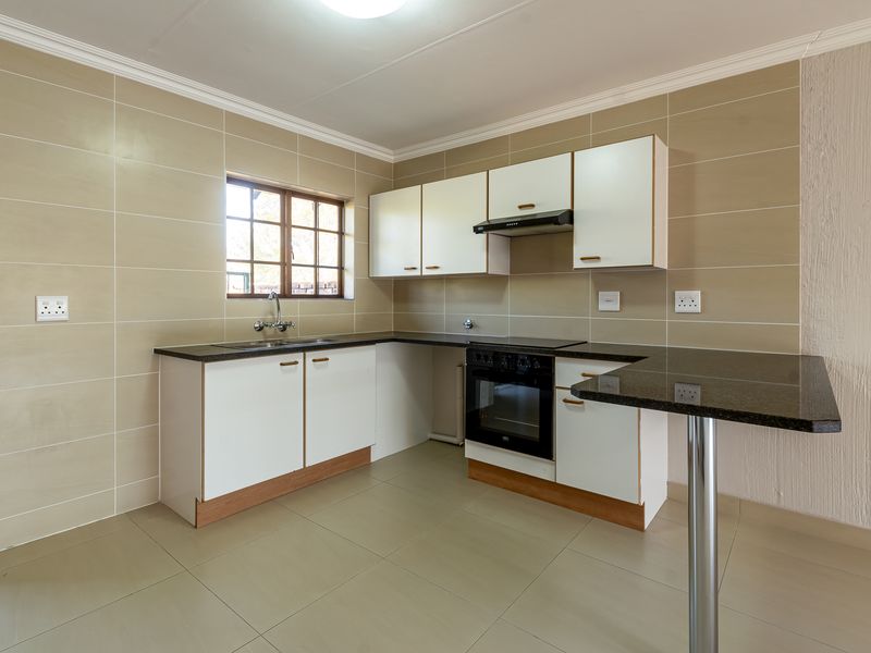 A clean, functional kitchen featuring white cabinetry, granite countertops, a breakfast bar, and built-in appliances, finished with neutral wall and floor tiles.