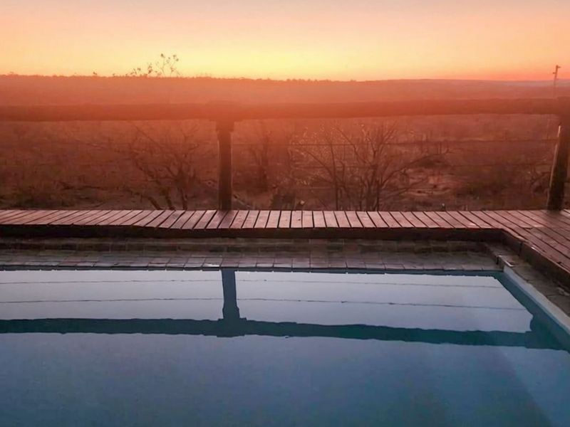 A swimming pool with timber decking and railing, overlooking a scenic landscape at sunset.