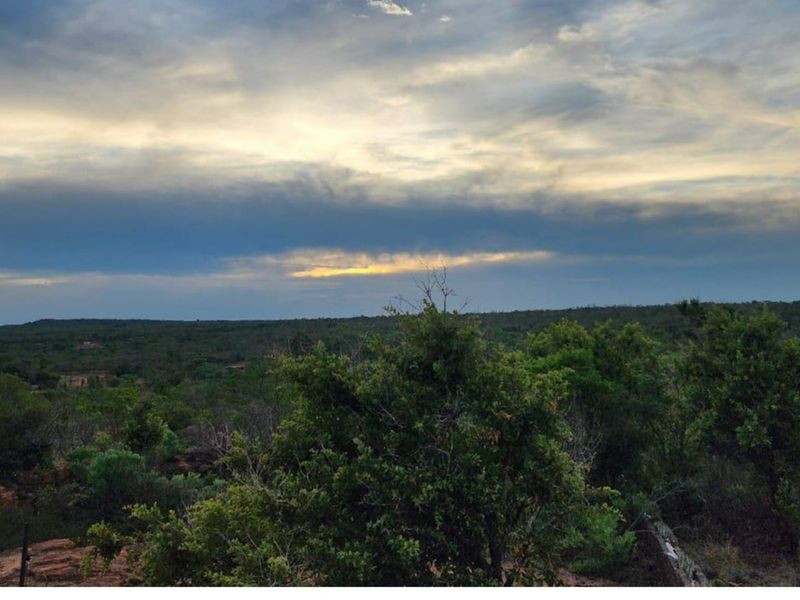 A scenic landscape view overlooking the natural bushveld and surrounding farm terrain under a dramatic cloudy sky.
