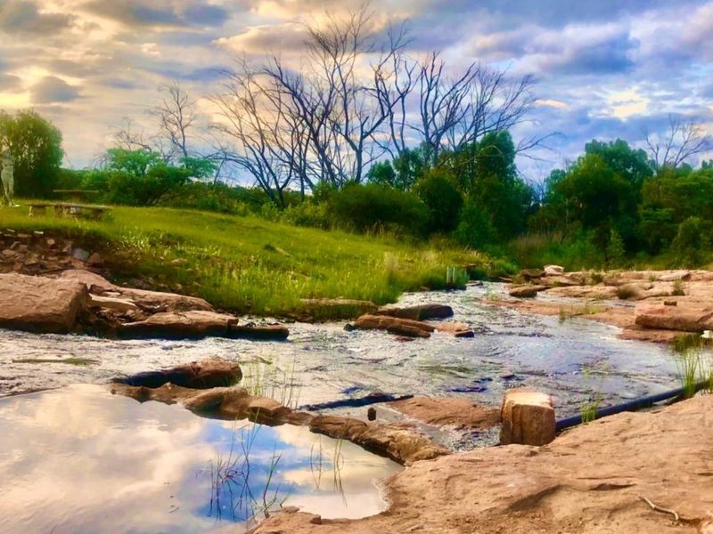A scenic view of a natural rocky stream flowing through the farm landscape under a dramatic cloudy sky.