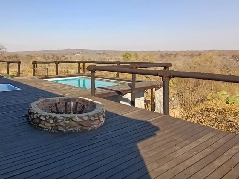 Expansive timber deck featuring a built-in stone fire pit and a swimming pool overlooking the surrounding bushveld landscape.