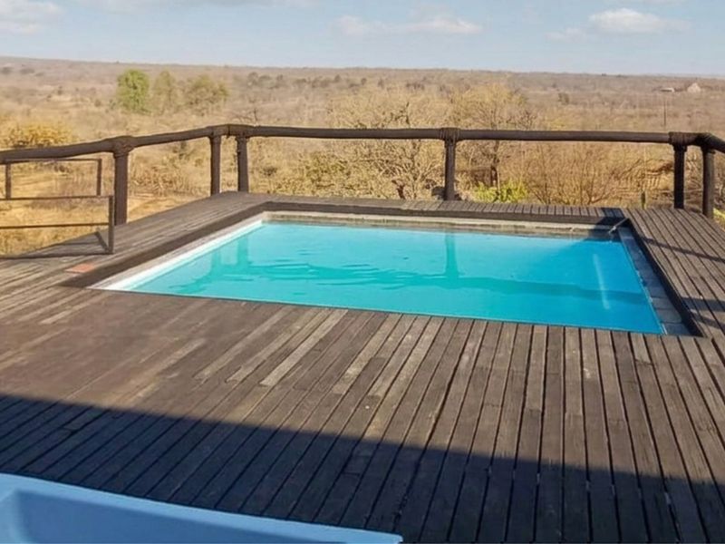 An elevated swimming pool featuring timber decking and a rustic timber railing, offering expansive views of the surrounding landscape.