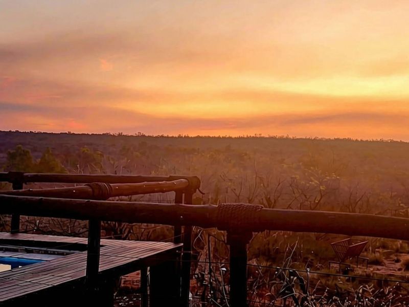 A scenic sunset view overlooking the landscape, featuring a wooden deck, timber railing, and a swimming pool.