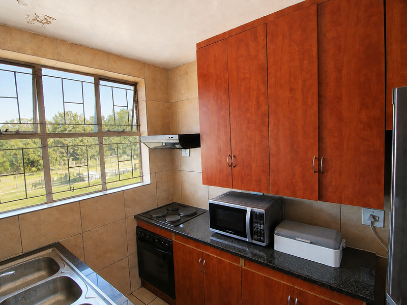 A functional kitchen featuring wood-finish cabinetry, granite countertops, a double basin sink, and built-in cooking appliances with large windows providing natural light.