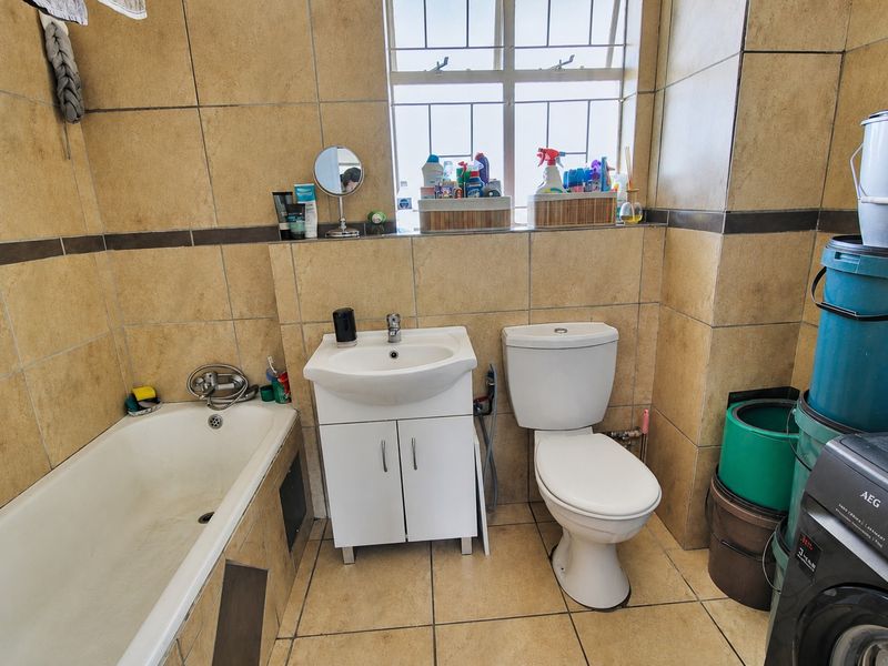 A functional bathroom featuring a bathtub, vanity basin, and toilet with full-height wall tiling and a window for natural light.