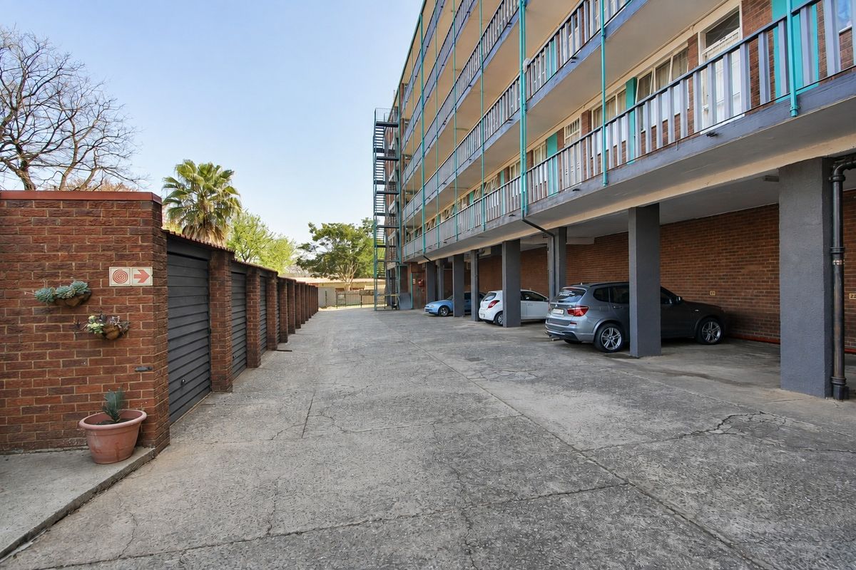 Rear view of the apartment building featuring a concrete driveway, covered parking bays, and access to ground-level garages and upper-floor balconies.