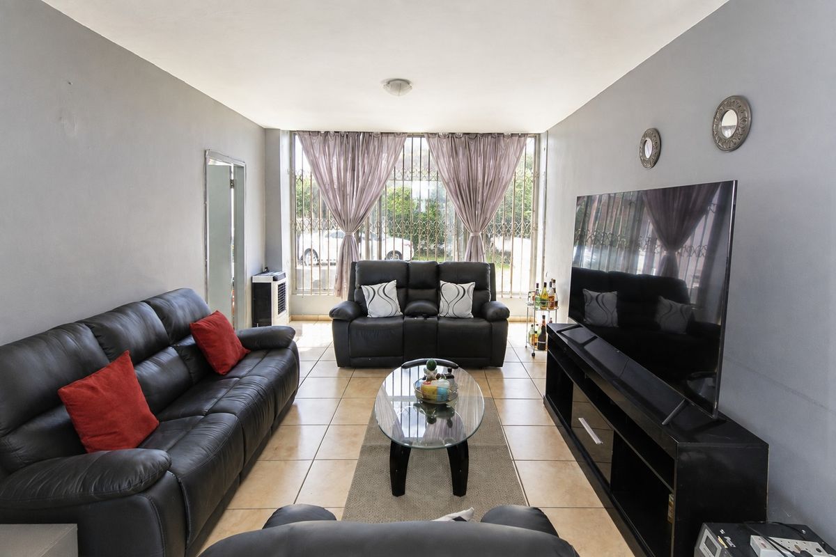 A well-lit living room featuring ceramic floor tiles and a large window secured with a metal security gate.