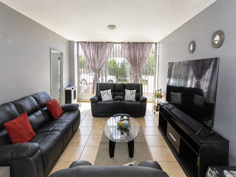 A well-lit living room featuring ceramic floor tiles and a large window secured with a metal security gate.