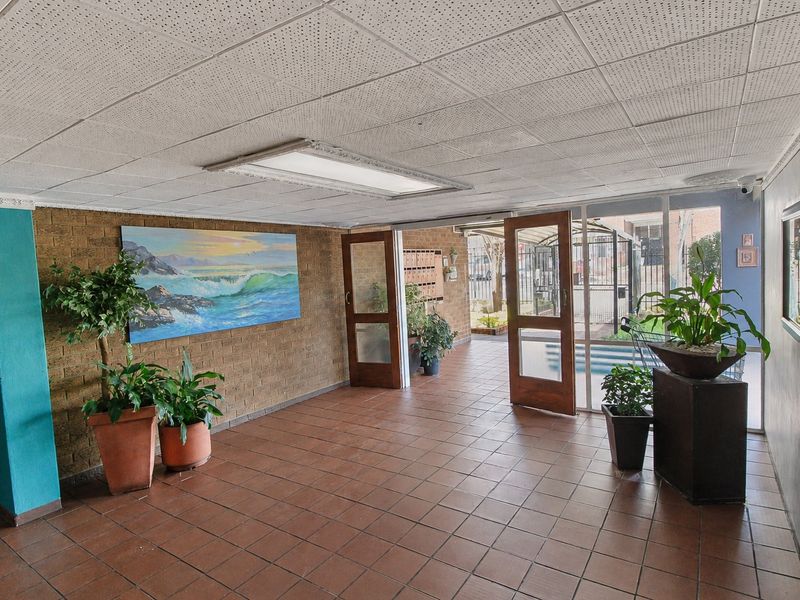 Spacious apartment building entrance lobby featuring tiled flooring, exposed brick walls, and a drop ceiling with integrated lighting.