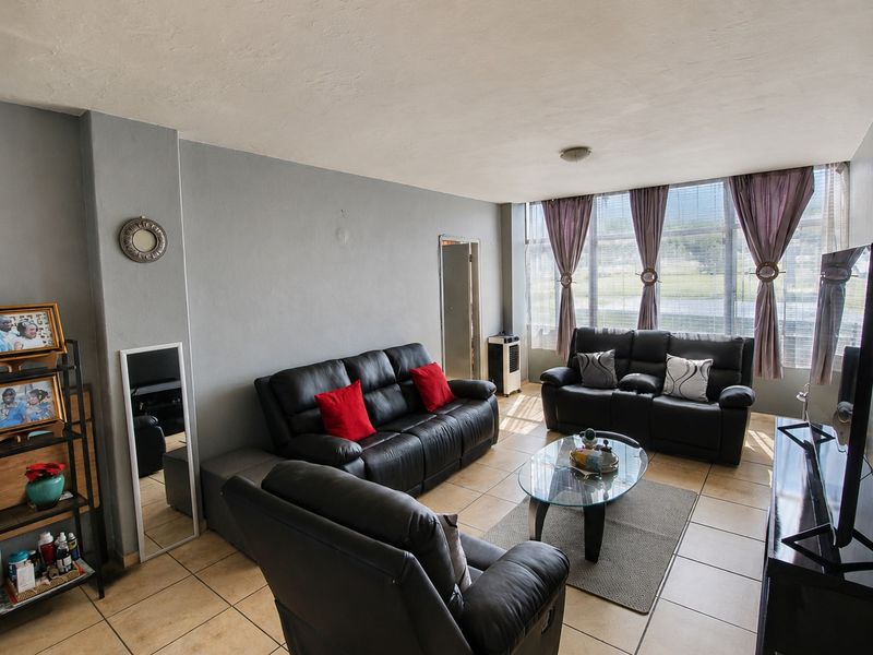 A spacious living room featuring large windows that provide ample natural light and neutral tiled flooring throughout the area.