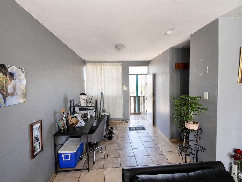 A living area featuring tiled flooring and an intercom system, with direct access to an exterior balcony through a security gate.