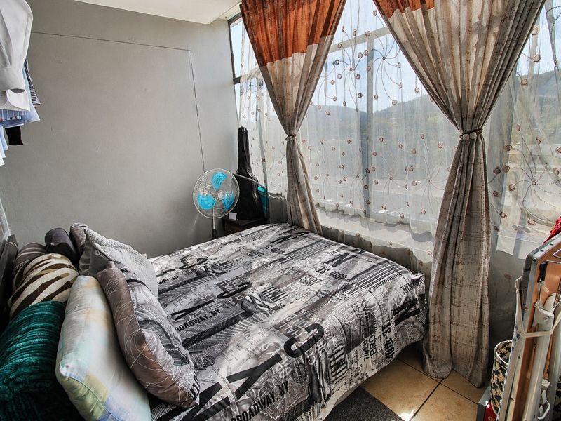 A compact bedroom featuring large floor-to-ceiling windows that provide natural light and views, finished with tiled flooring.