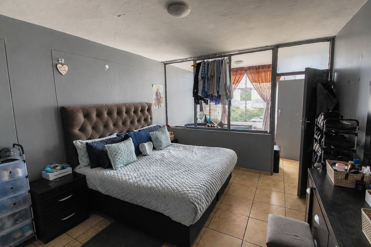 A bedroom featuring tiled flooring and a large internal window partition, offering a functional layout with potential for cosmetic updates.