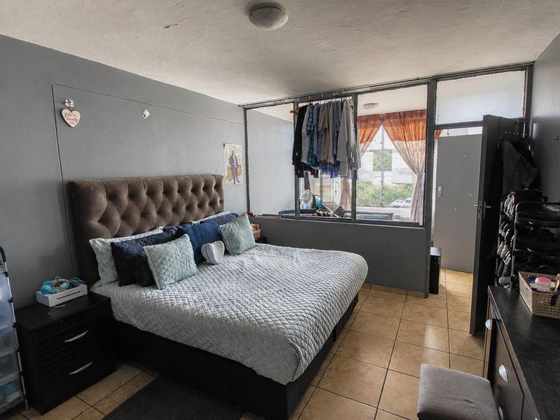 A bedroom featuring tiled flooring and a large internal window partition, offering a functional layout with potential for cosmetic updates.