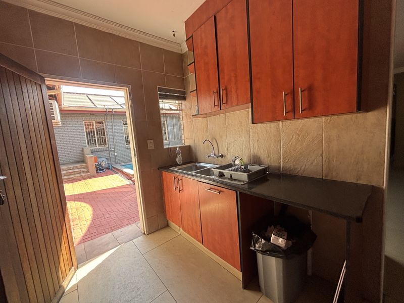 A functional scullery area featuring built-in wooden cabinetry, a double basin sink, and direct access to the rear patio and garden area.