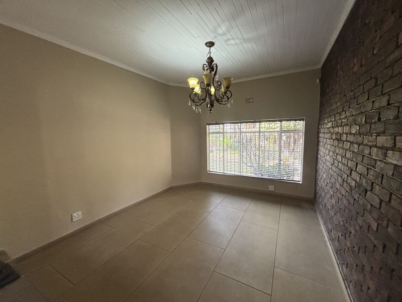 Spacious living area featuring a striking exposed brick wall, tiled flooring, and a classic chandelier, offering a versatile blank canvas for interior design.