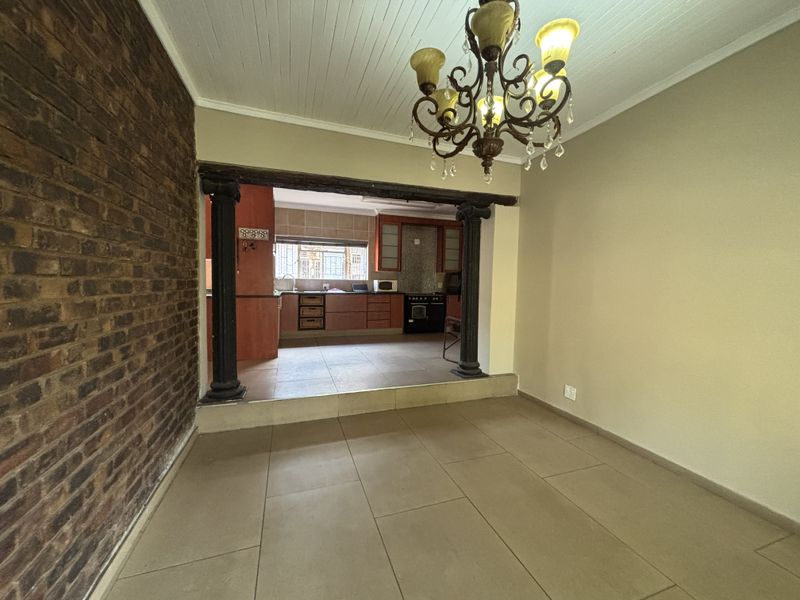 Open plan living and kitchen area featuring exposed brickwork, decorative columns, tiled flooring, and a classic chandelier, offering a versatile space for dining or relaxation.