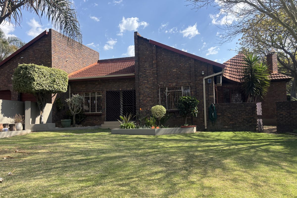 A well-maintained face brick house featuring a tiled roof, security bars on windows, and a spacious, landscaped rear garden.