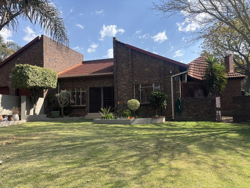 A well-maintained face brick house featuring a tiled roof, security bars on windows, and a spacious, landscaped rear garden.