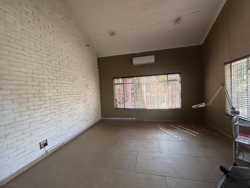 Spacious living area featuring a vaulted timber ceiling, exposed white brick wall, tiled flooring, and a wall-mounted air conditioning unit.