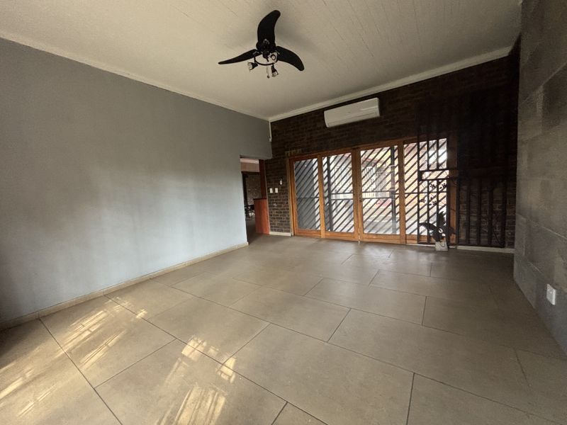 Spacious living area featuring large format floor tiles, an exposed brick feature wall, ceiling fan, air conditioning, and sliding doors leading to the exterior.