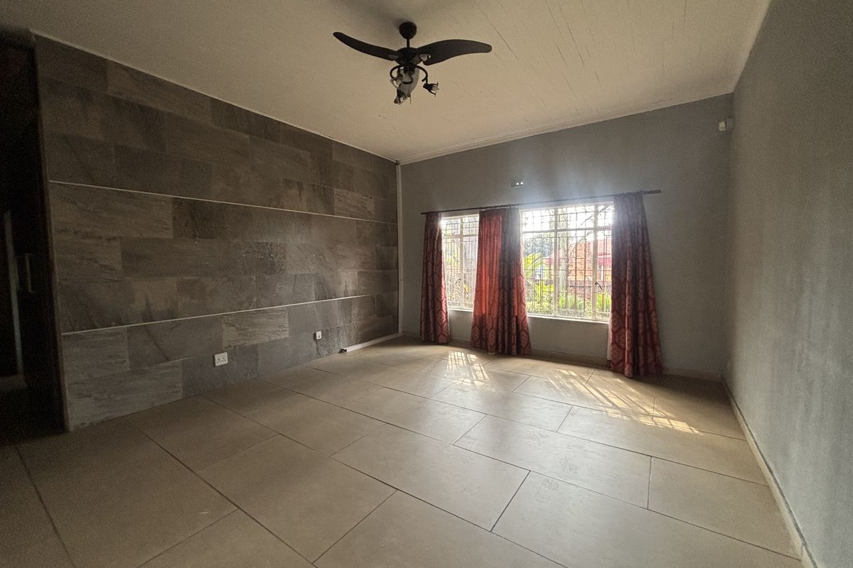 Spacious living room featuring large format floor tiles, a stone accent wall, and a ceiling fan, offering a clean and neutral canvas.
