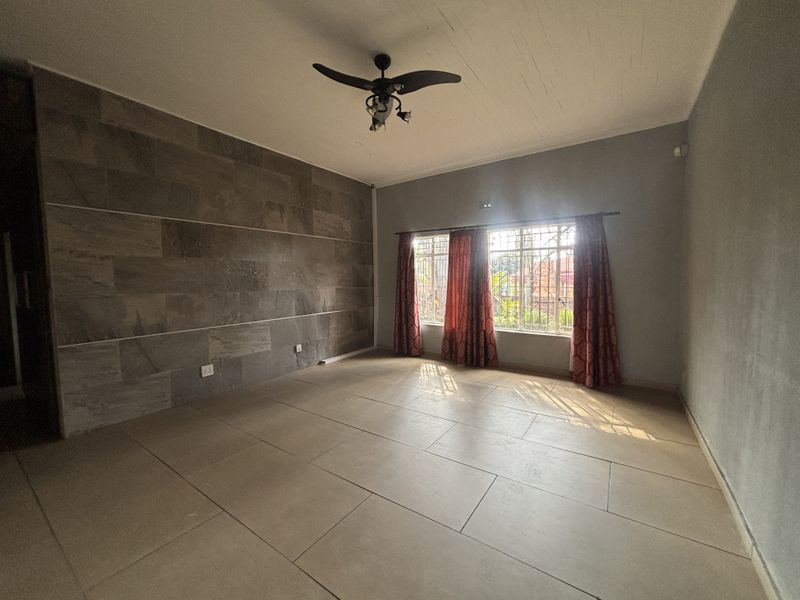 Spacious living room featuring large format floor tiles, a stone accent wall, and a ceiling fan, offering a clean and neutral canvas.