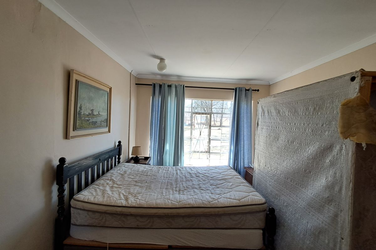 A bedroom featuring a steel window frame with security gate, coved ceilings, and dated wall finishes, offering potential for cosmetic renovation.
