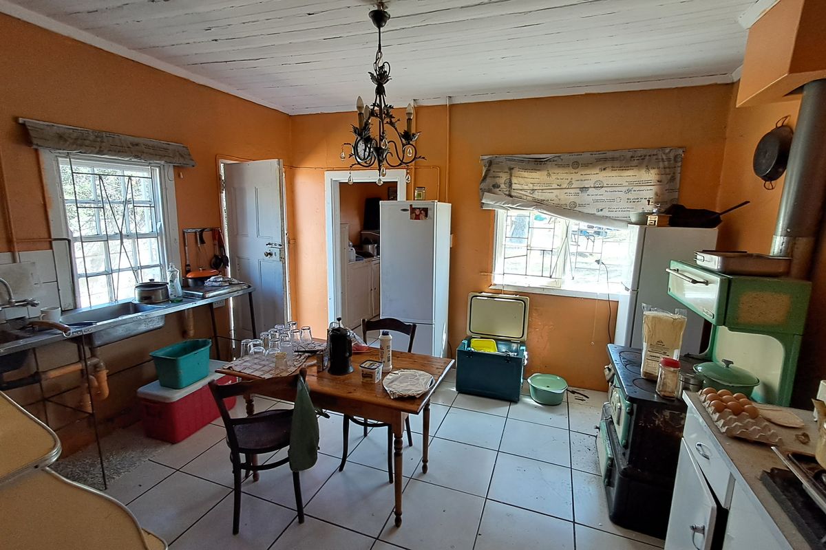 A rustic kitchen featuring a vintage wood-burning stove, tiled flooring, and exposed timber ceiling, offering significant potential for renovation and modernization.
