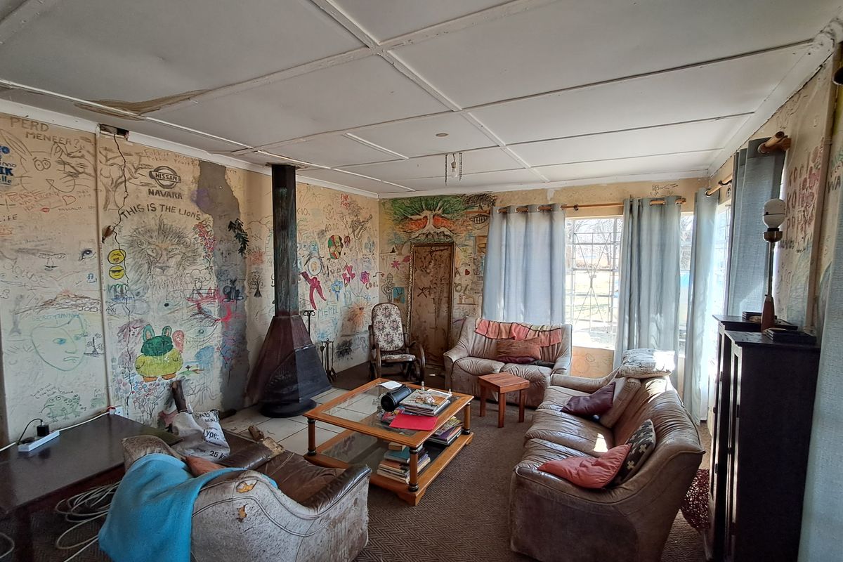 Living room featuring a freestanding fireplace and large windows, currently requiring significant cosmetic renovation due to extensive wall damage and graffiti.