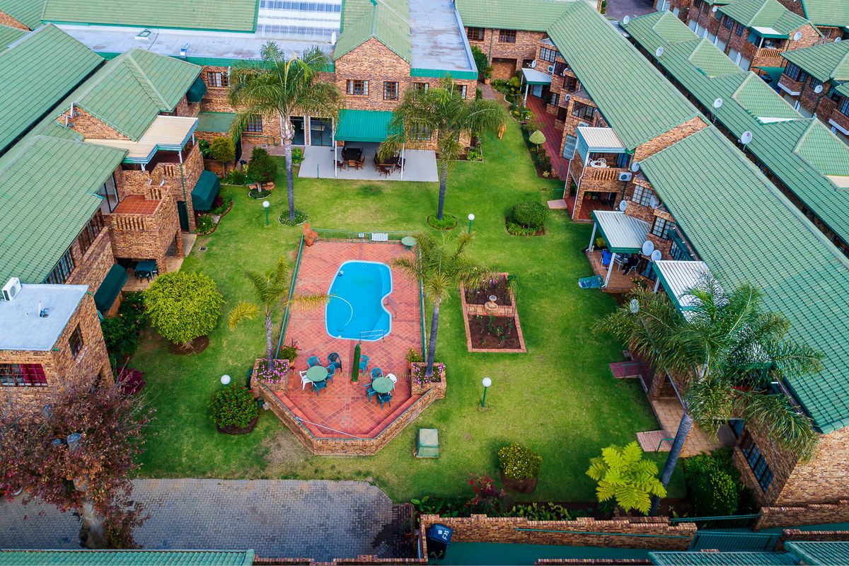 Aerial view of a townhouse complex featuring a central communal garden, swimming pool, paved patio areas, and brick buildings with green tiled roofs.
