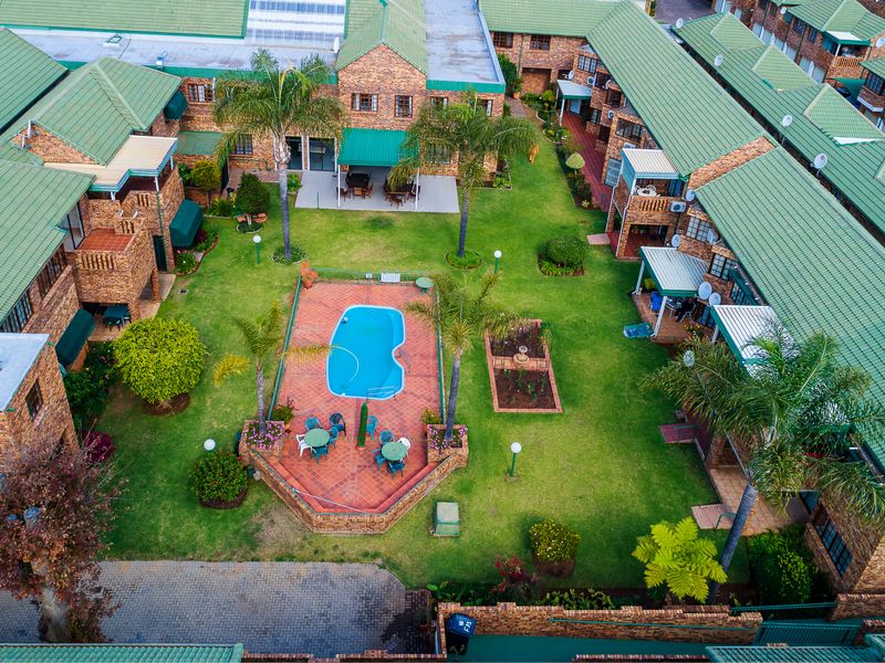 Aerial view of a townhouse complex featuring a central communal garden, swimming pool, paved patio areas, and brick buildings with green tiled roofs.