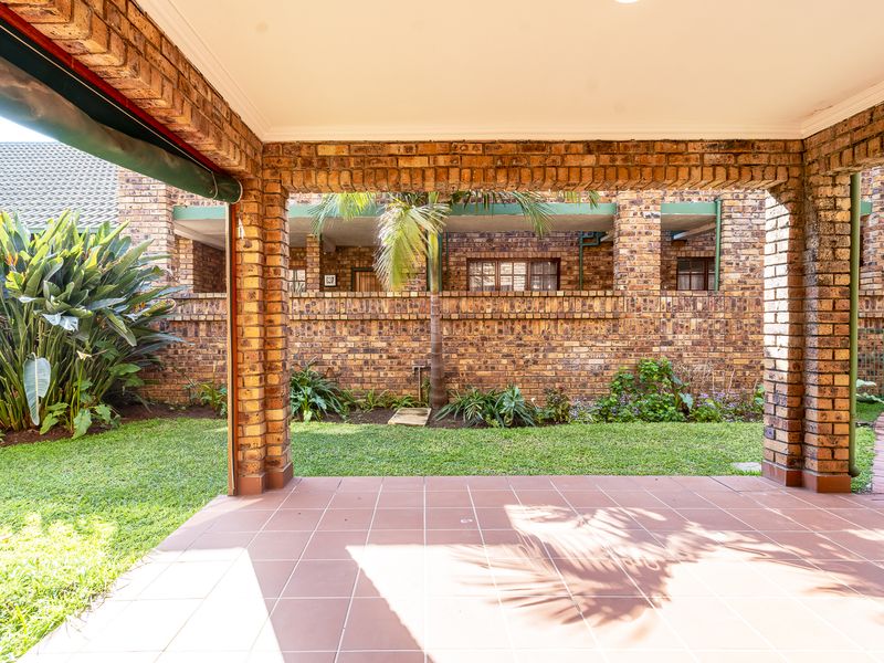 A covered patio area featuring exposed brick pillars, tiled flooring, and a retractable awning, overlooking a private garden space.