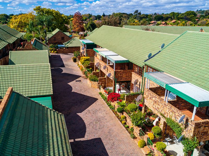 Aerial view of a townhouse complex featuring brick facades, green tiled roofs, and paved driveways within a landscaped residential estate.