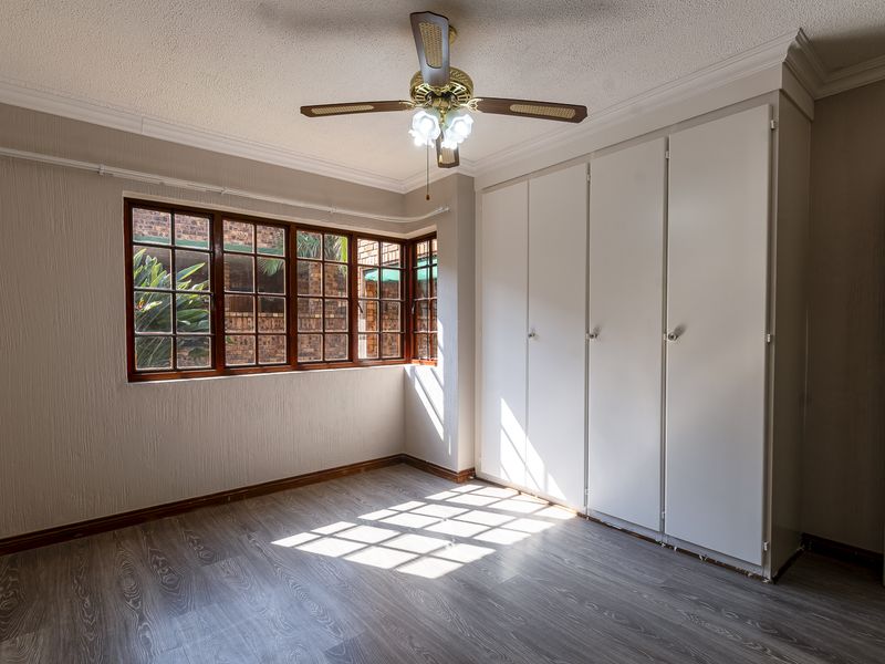A bright, empty bedroom featuring built-in cupboards, a ceiling fan, and modern laminate flooring, offering a clean canvas for personalization.