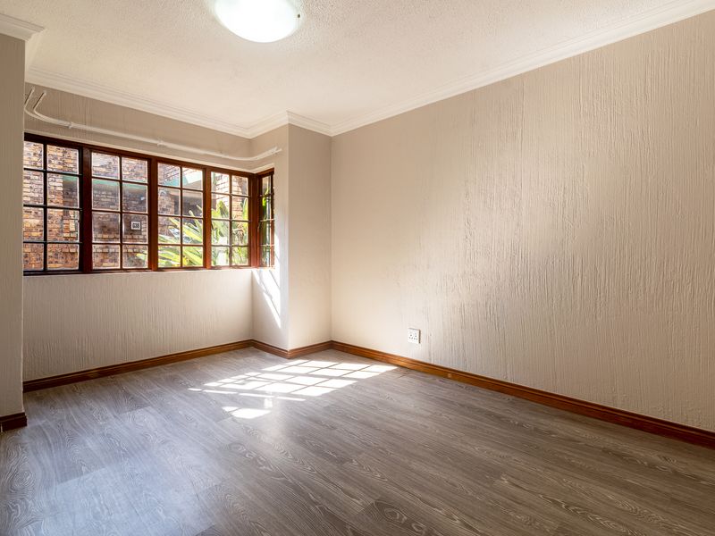 A bright, empty bedroom featuring laminate flooring, timber-framed windows, and textured wall finishes, offering a clean canvas for personalization.