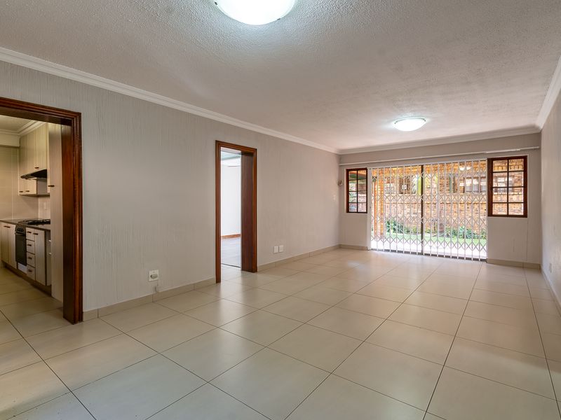 A spacious, empty living room featuring neutral tiled flooring, coved cornicing, and a security gate leading to the outdoor area.