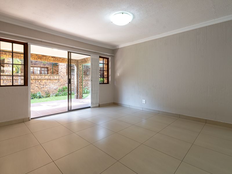 An empty, well-lit living room featuring neutral tiled flooring, textured walls, and a sliding glass door providing direct access to an outdoor patio area.