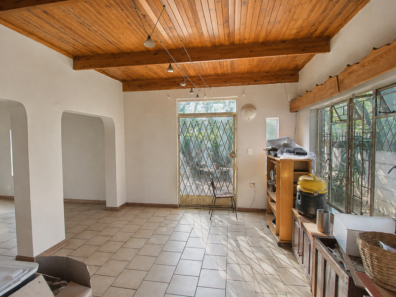 Spacious living area featuring a warm timber-clad ceiling with exposed beams, ceramic tiled flooring, and large steel-framed windows leading to a secure exterior entrance.