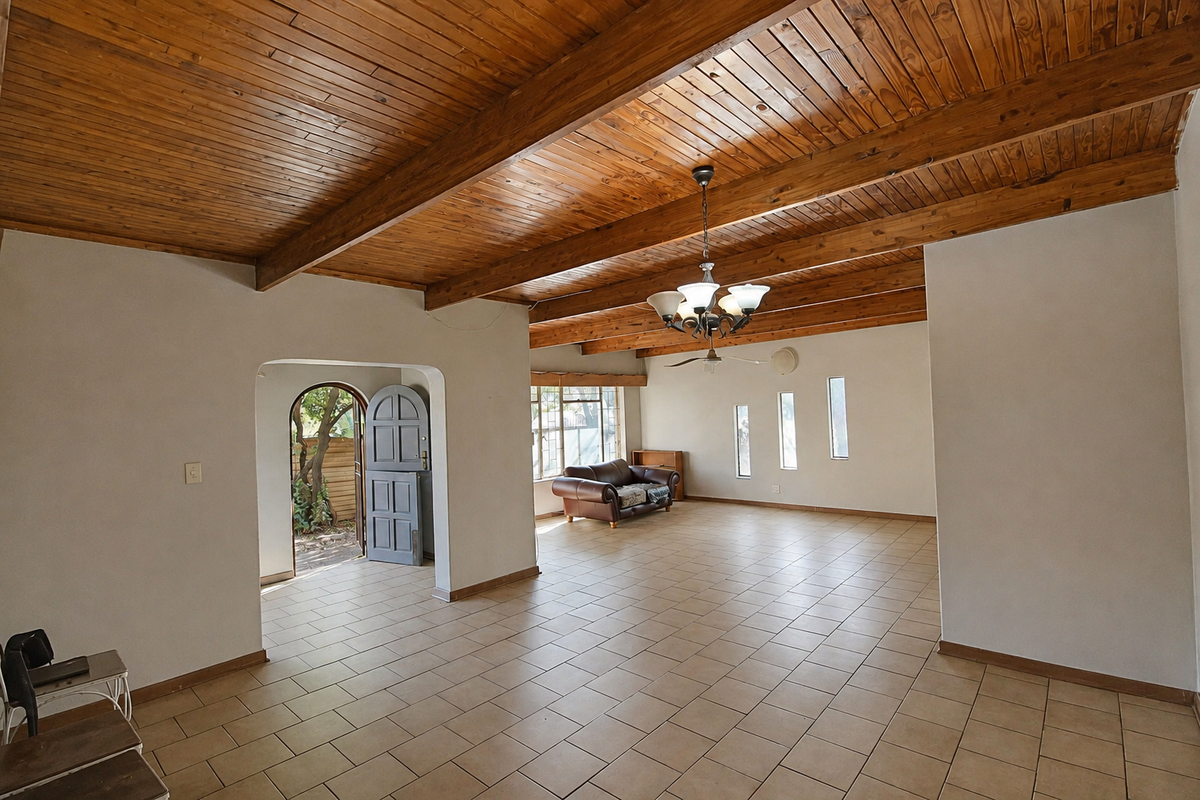 Spacious living area featuring high exposed timber beam ceilings, neutral tiled flooring, and an arched doorway leading to the exterior.