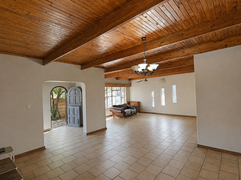 Spacious living area featuring high exposed timber beam ceilings, neutral tiled flooring, and an arched doorway leading to the exterior.