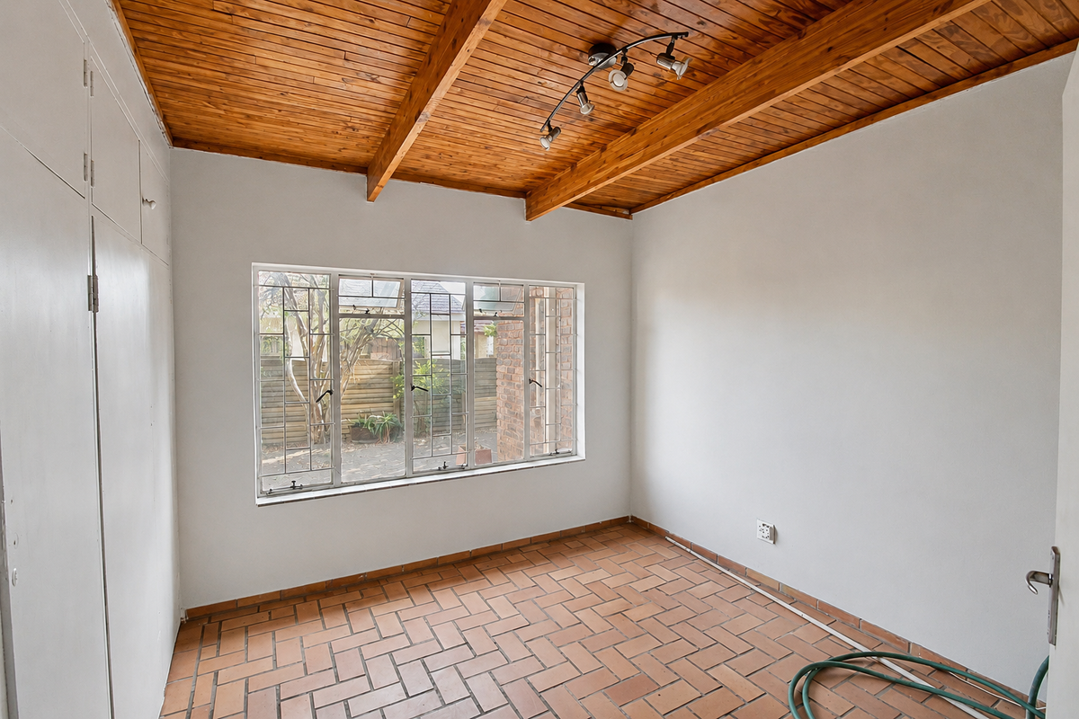 An empty bedroom featuring a warm timber-clad ceiling, terracotta tiled flooring, and built-in storage cupboards, offering a blank canvas for personalization.